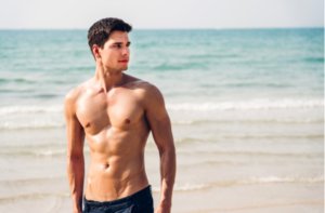 handsome sexy man showing muscular fit body standing on the tropical beach