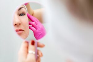 Woman examines her face in a mirror beside medical professionals after rejuvenating her appearance with facelift