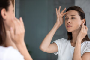 Woman gazes at reflection, pondering brow lift in Worcester, MA