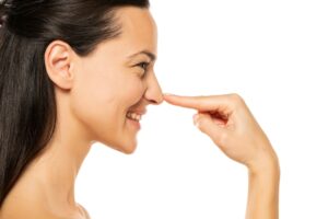 Side profile of woman who smiles playfully as she touches her nose while considering a personalized nose job.