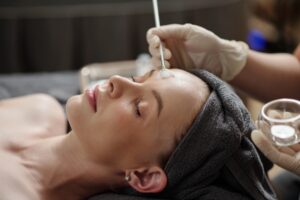 Dermatologist applying a chemical peel with a brush on a woman’s face to exfoliate skin and improve complexion.