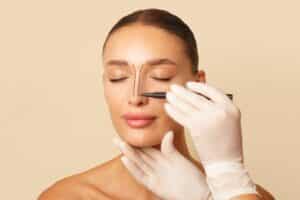 Plastic surgeon marking a young woman’s nose during a pre-surgical consultation, illustrating the planning phase of a rhinoplasty procedure. Patient appears calm with eyes closed, highlighting trust and preparation
