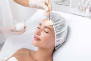 Woman receiving rejuvenation treatment, facial chemical peel therapy in beauty salon or medical center.
