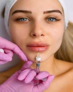 Close-up of lip augmentation injection procedure with cosmetologist applying dermal filler for facial rejuvenation, youth, and beauty