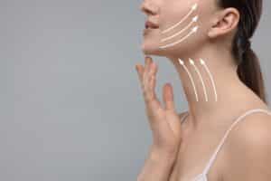 Woman with perfect skin after cosmetic treatment on grey background, space for text. Lifting arrows on her neck and face