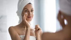 Woman applying lotion to face while looking in the mirror after Botox treatment.