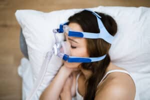 Woman wearing CPAP machine to sleep with sleep apnea due to obstructed nasal airflow.